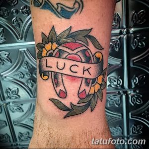 Фото тату: Традиционная татуировка подковы с лентой, на которой написано 'Luck', и цветами. Яркий и красочный дизайн.