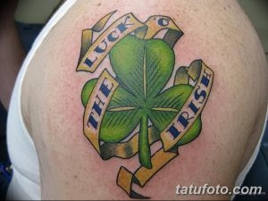 Фото тату: Цветная татуировка ирландского клевера с лентами и надписью 'Luck the Irish' на плече. Классический дизайн, символизирующий удачу.