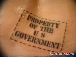 Фото тату: штамп 'PROPERTY OF THE US GOVERNMENT' на коже. Необычный и ироничный рисунок татуировки, выполненный в черном цвете.