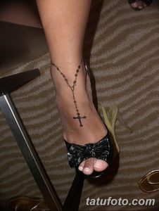 Фото тату: черная татуировка в виде четки, обвивающей лодыжку. Эскиз татуировки выполнен тонкими линиями, с акцентом на крестик.