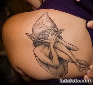 Фото тату с изображением Домовика, существа из Гарри Поттера, выполненное на плече. Рисунок выполнен в черно-белой гамме с использованием детализации.