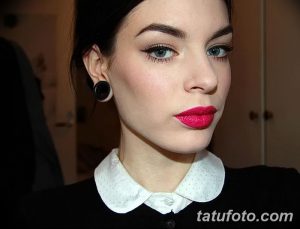 Фотография девушки с черными тоннелями в ушах и ярким макияжем: красная помада и выразительные глаза. Классический стиль одежды.