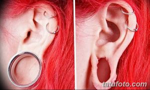 Фотография девушки с красными волосами и растянутыми ушами, украшенными металлическими кольцами. Видны также пирсинги в хряще уха.