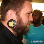 Мужчина с длинной бородой и растянутой мочкой уха, в которой вставлен плаг с логотипом Apple. Фото сделано в магазине Apple.