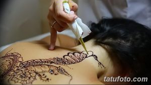 Фото процесса нанесения тату мехенди на спину, демонстрирующее работу мастера с конусом хны и создание сложного узора.