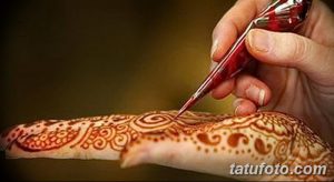 Фото процесса нанесения тату мехенди на руку, демонстрирующее работу мастера с конусом хны и создание изящного узора.