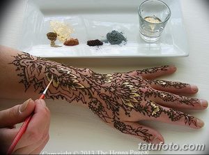 Фотография роскошной татуировки хной на руке, украшенной золотыми акцентами. Мастер наносит последние штрихи.