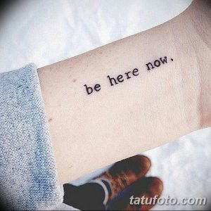 Черно-белое фото татуировки с надписью 'be here now' на предплечье. Простой, но вдохновляющий рисунок татуировки.