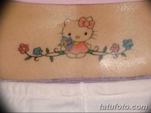 Фото тату Hello Kitty с цветами на теле. Цветная татуировка в стиле аниме, выполненная с использованием ярких оттенков.