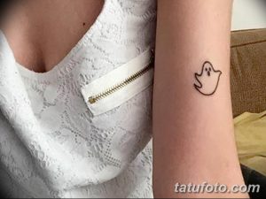 Фото тату: маленький рисунок привидения с милым выражением лица, выполненный черными линиями на запястье. Забавный эскиз татуировки.