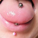 Фото тату пирсинга языка с серебристым шариком и дополнительным розовым пирсингом на губе. Крупный план демонстрирует оба украшения.