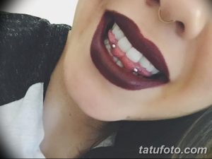 Фото пирсинга языка на фоне яркой помады. Крупный план демонстрирует прокол и выразительный макияж губ.