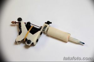 Фотография современной тату-машинки с белым корпусом и иглой. Видны детали конструкции и крепления.