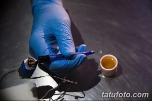 Фотография процесса подготовки краски для татуировки и тату-аппарата в руках мастера в перчатках. Изображение демонстрирует профессиональный подход к татуировке.
