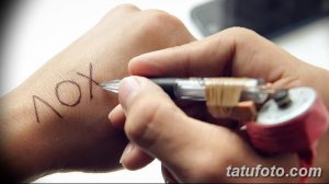Фотография процесса нанесения надписи "лох" на руку с помощью самодельной тату-машинки. Изображение демонстрирует рискованный способ нанесения татуировки.