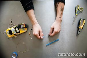 Фото тату: руки мастера разбирают и собирают тату-машинку. Рядом с руками расположены детали машинки, провода, инструменты и игрушечная машинка.