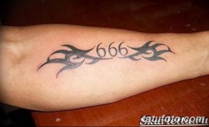 Фото татуировки с числом 666 в стиле трайбл на предплечье. Чёрный рисунок, выполненный с использованием геометрических узоров и острых линий.
