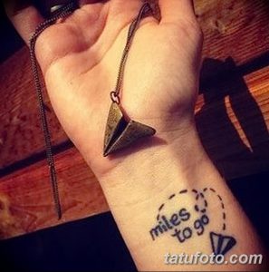 Фото тату бумажного самолетика на запястье с надписью 'miles to go'. Черно-белый рисунок, минимализм, вдохновляющий дизайн.