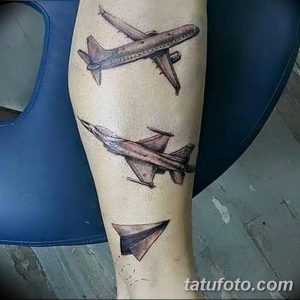 Фото татуировки на руке, изображающей несколько самолетов, включая бумажный самолетик. Тату выполнена в реалистичном стиле с использованием серых оттенков.
