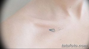 Фото тату: маленький бумажный самолетик, выполненный в технике дотворк на ключице. Черно-белый рисунок татуировки.