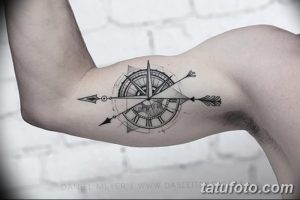 Черно-белая татуировка на предплечье, изображающая компас и стрелу. Стиль - тонкие линии и минималистичный дизайн.
