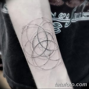 Черно-белая татуировка на предплечье, выполненная в геометрическом стиле. Изображены переплетающиеся круги и треугольники, создающие сложный узор.