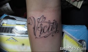 Фото тату с именем "Victor" на предплечье. Каллиграфический стиль, выполненный черными чернилами. Элегантный и изящный рисунок татуировки.