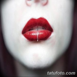 Фото пирсинга нижней губы с тонким серебристым кольцом на фоне яркого красного макияжа и бледной кожи. Идеи для готического пирсинга.