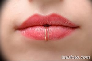 Фотография демонстрирует пирсинг нижней губы с использованием двух золотистых колец. Кольца расположены в центре нижней губы.