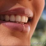 Фотография демонстрирует пирсинг нижней губы с использованием небольшого серебристого кольца. Пирсинг расположен сбоку от центра губы.