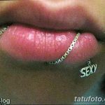 Крупный план губы с проколом, украшенным цепью и подвеской с надписью "SEXY". Фото демонстрирует провокационный и привлекательный образ.
