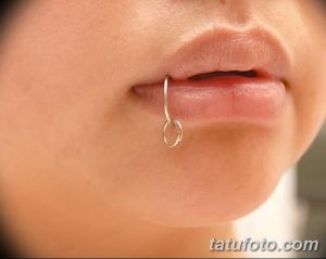 Фото пирсинга губы с серебряным кольцом. Крупный план женской губы с аккуратным пирсингом в центре нижней губы. Стильный и минималистичный дизайн.