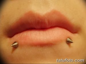 Фотография нижней губы с двумя черными шипами в качестве пирсинга, на фоне светлой кожи.