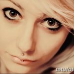 Фотография молодой девушки с пирсингом губы и носа, с акцентом на ее выразительные глаза и светлые волосы.