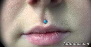 Фото пирсинга нижней губы с одним бирюзовым украшением. Крупный план, акцент на форме губ и цвете украшения. Идеи для пирсинга губ.