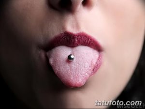 Фотография языка, проколотого вертикально. Виден серебряный металлический пирсинг. Крупный план демонстрирует необычный вид модификации.