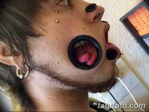 Фотография мужчины с пирсингом губ, щек и языка. Видны металлические украшения и большие растяжки в губах.