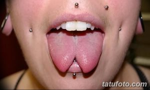 Крупный план рта женщины с разделенным языком и множеством пирсингов. Демонстрация экстремальной боди-модификации.