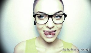 Фотография девушки с разделенным языком и пирсингом. Она надета в желтую майку и очки в черной оправе.