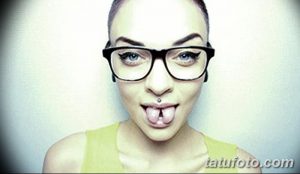 Фотография девушки в очках с татуировкой на нижней губе. Смелый и провокационный образ, привлекающий внимание.