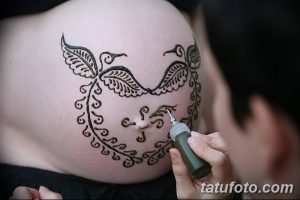 Фото тату хной на животе беременной женщины: изображение птицы с расправленными крыльями, окруженное растительным орнаментом. Символ материнства и надежды.