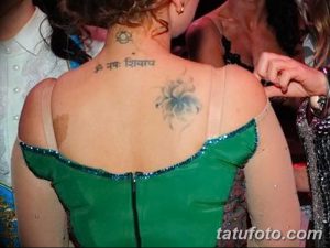 Фотография девушки в зеленом платье, демонстрирующей татуировку на шее и спине. Элегантный и загадочный образ.