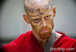 Фотография мужчины с татуировками, покрывающими его лицо. Татуировки выполнены в темных тонах и создают сложный и пугающий образ.