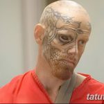 Фотография мужчины с татуировками, покрывающими его лицо и шею. Татуировки выполнены в темных тонах и создают мрачный и угрожающий образ.