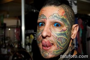 Фотография мужчины с татуировками, покрывающими его лицо, и высунутым языком. Изображение демонстрирует экстремальный стиль модификации тела.