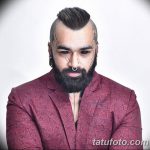 Фото мужчины с татуировками на висках и щеках, а также с аккуратной бородой и стильной прической. Современный и модный образ.