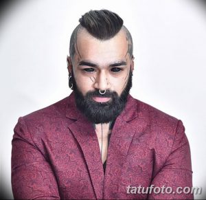 Фото мужчины с татуировками на висках и щеках, а также с аккуратной бородой и стильной прической. Современный и модный образ.