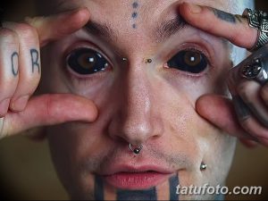 Фото мужчины с множеством татуировок на лице, пирсингом и необычными модификациями тела. Экстремальный и вызывающий образ.