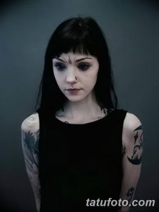Фотография девушки с лиловыми глазами и татуировкой на руке. Черные волосы и серьезный взгляд.