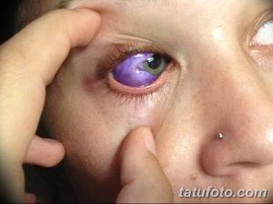 Фото тату: девушка с фиолетовой радужной оболочкой глаза, созданной с помощью татуировки. Крупный план лица, акцент на глазах.
